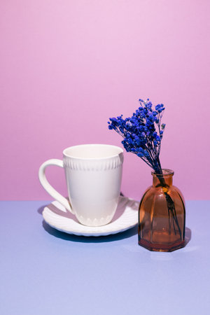 White coffee cup with vase of blue dry flowers on blue table. pink wall backgroundの写真素材