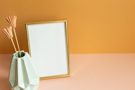 Blank photo frame with vase of dry flowers on pink table. orange wall background. copy spaceの写真素材