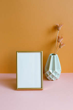 Blank photo frame with vase of dry flowers on pink table. orange wall background. copy spaceの写真素材