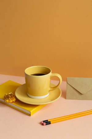 Yellow diary notebook, cup of coffee, pencil on pink desk. orange wall background. copy spaceの写真素材