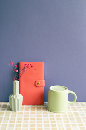 Notebook and coffee cup, dry flower on desk. purple wall background. workspace