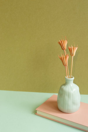 Pink notebook and vase of dry flower on sky blue desk. khaki wall backgroundの写真素材
