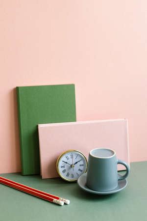 Notebook, clock, coffee cup, pencil on green desk. pink wall background. workspaceの写真素材