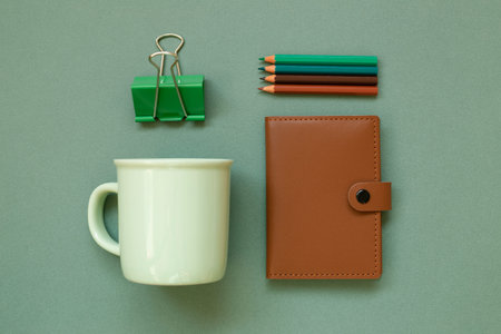 Notebook, pencil, clip, mug cup on green background. workspace. flat lay, top view, copy space