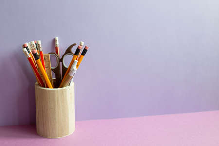 Pencils and various stationery in wooden holder on purple desk. purple wall backgroundの写真素材
