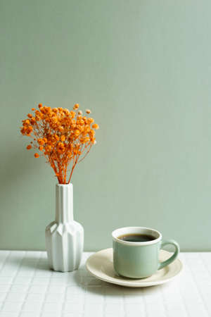 Cup of coffee and orange dry flowers on white table. khaki green wall backgroundの写真素材