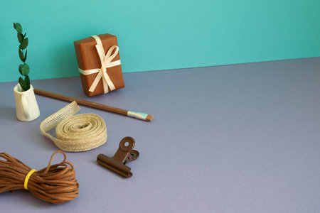 Gift box, ribbon roll, plant on purple table. blue background