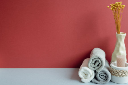 Stack of rolled shower cotton towels and candle, vase of dry flower. bathroom spa concept. red and gray backgroundの写真素材