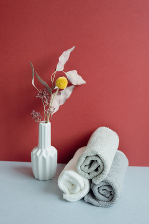 Stack of rolled shower cotton towels and vase of dry flower. bathroom spa concept. red and gray backgroundの写真素材