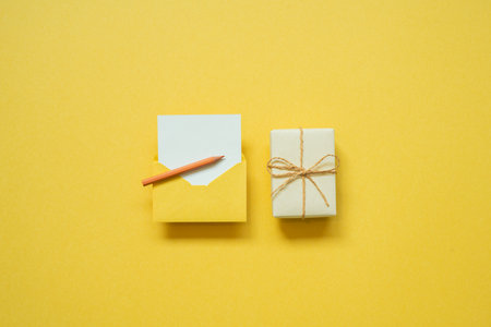 Gift box and envelope with white blank card on yellow background. top view, copy space, minimalismの写真素材