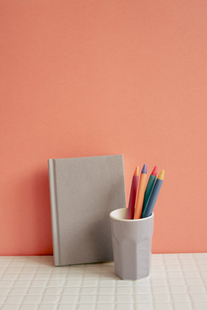 Notebook and pen holder on white desk. pink wall background. workspaceの写真素材