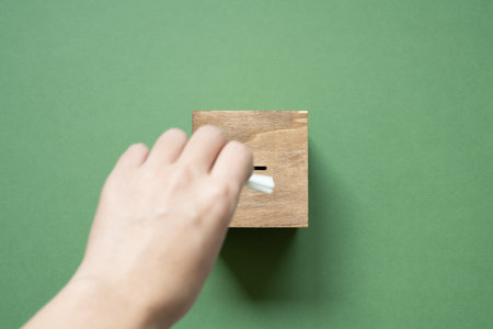 Hand putting wooden ballot voting box on green background. top viewの写真素材