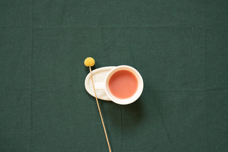 Cup of pink tea and yellow flower on green fabric table background. top view, copy spaceの写真素材