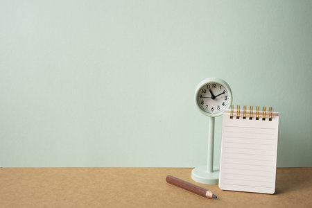 Notebook, colored pencil, clock on brown desk. mint green wall background. workspace, copy space