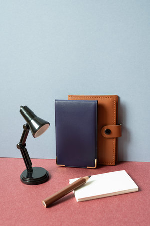 Study and workspace. Notebook, lamp, colored pencil, memo pad on red desk. gray wall background