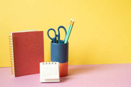 Notebook, pencil holder, calender on pink desk. yellow background. workspaceの写真素材