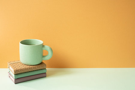 Stack of notebook and mug cup on mint green desk. orange background. copyspaceの写真素材