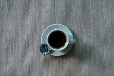 Cup of coffee with dry flower on gray fabric background. top view, copy space