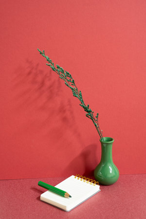 Notepad and colored pencil with vase of plant on red desk. red wall backgroundの写真素材