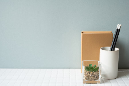 Working desk with notebook, pencil holder, potted plant on white tile desk. gray wall backgroundの写真素材