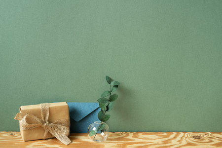 Kraft paper gift box, blue envelope, eucalyptus on wooden table. green wall backgroundの写真素材