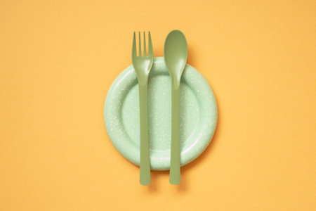 Empty green plate and cutlery on orange table background. Flat lay, top view