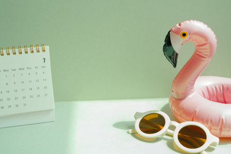 Summer vacation planning concept. Pink flamingo bird shape swimming pool tube and sunglasses, calendar on mint green backgroundの写真素材