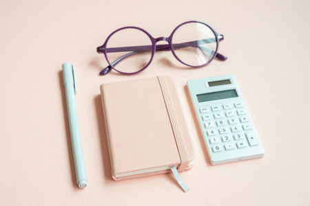 Diary notebook, pen, eyeglasses, calculator on pink desk backgroundの写真素材