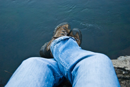 crossed legs of man on waters of a blue river