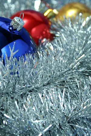 Three christmas sparkling spheres of dark blue, yellow and red color on a background of a silvery New Year's tinselの写真素材