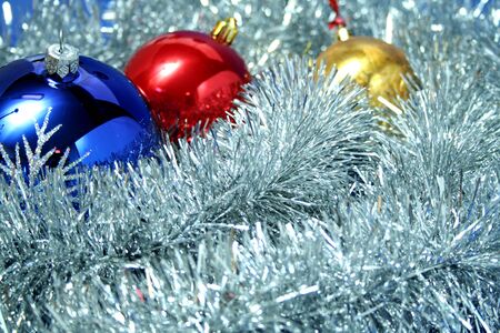 Three celebratory sparkling spheres of dark blue, yellow and red color on a background of a silvery New Year's tinselの写真素材
