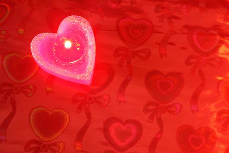 Candle in the form of heart on a red background の写真素材