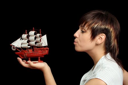 The nice girl blows on a toy ship in a hand, isolated on black backgroundの写真素材