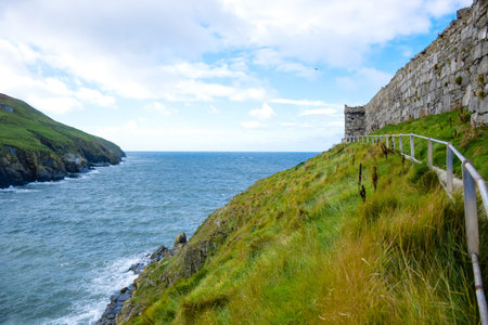 Beautiful coastline with green grass and great wall of Peel Castle in Peel, Isle of Man.のeditorial素材