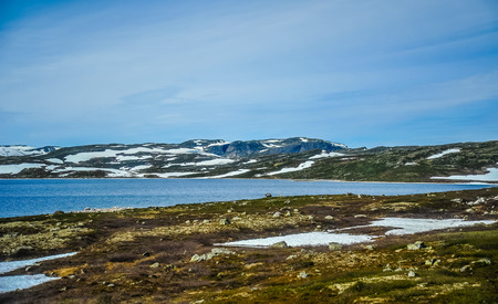 Beautiful landscape and scenery of Norway, the hills and mountain covered partially with white snow and blue lakeの写真素材