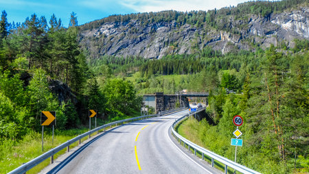 Long empty road through the beautiful scenic view of Norway surrounded by green mountain hill in the sunshine clear blue sky dayの写真素材
