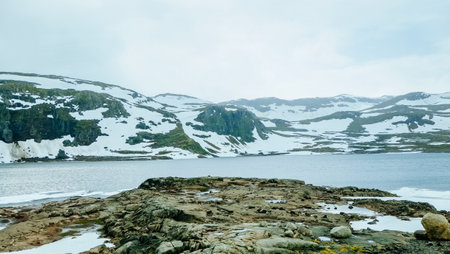 Winter nature landscape of snowcapped mountain hill and lake covered with ice snow in Norway countrysideの写真素材