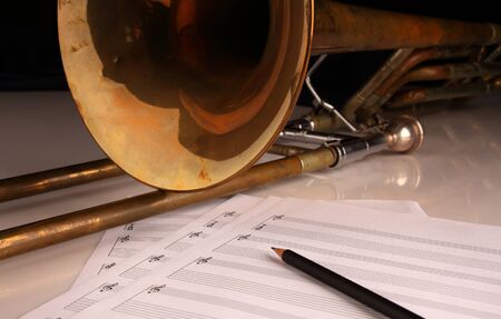 Vintage trombone, pencil and sheet music on a glossy white table and dark backgroundの写真素材
