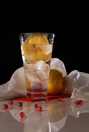 Glass of water with ice cubes and lemon on a dark backgroundの写真素材