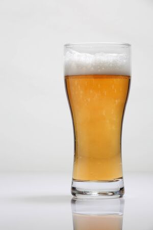 A large glass of beer on a glossy table and a light backgroundの写真素材