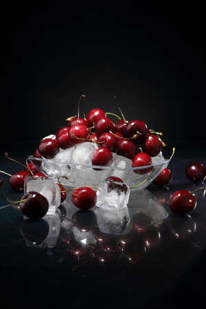 Cherry berries in a vase with ice on a glossy table and a dark backgroundの写真素材