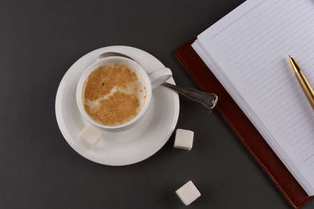 A Cup of coffee with sugar and a notebook with a pen on a gray backgroundの写真素材