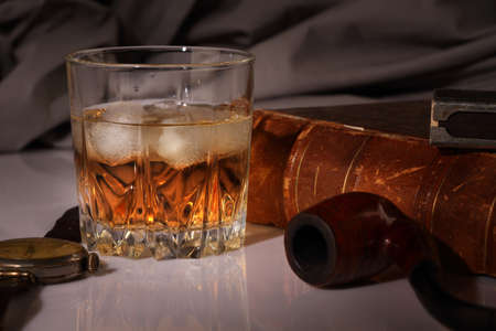 A glass of whiskey with a Smoking pipe, a watch and an antique book on a gray backgroundの写真素材