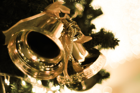 golden bells with a red bow on Christmas tree blur bright bokeh backgroundの写真素材