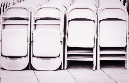 Dozens of fold up white metal chairs stacked .outdoor Party.