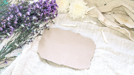 Blank craft paper and flower decoration. Greeting card on a white natural; linen background. Top view. Copy space.の写真素材