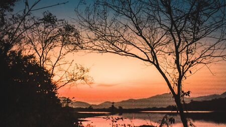 Landscape with orange and purple at sunset  silhouettes of mountains, hills and forest lakeの写真素材