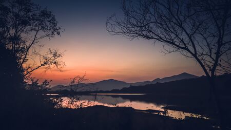 Landscape with orange and purple at sunset  silhouettes of mountains, hills and forest lakeの写真素材