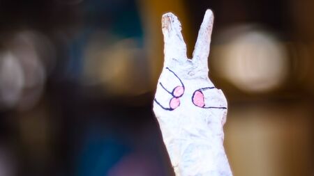 Hand showing peace gesture through torn yellow paper background. Victory, V sign. Two fingers victory peace sign body languageの写真素材