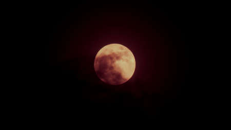 red full moon behind shadow of cloud in dark sky night time.の写真素材